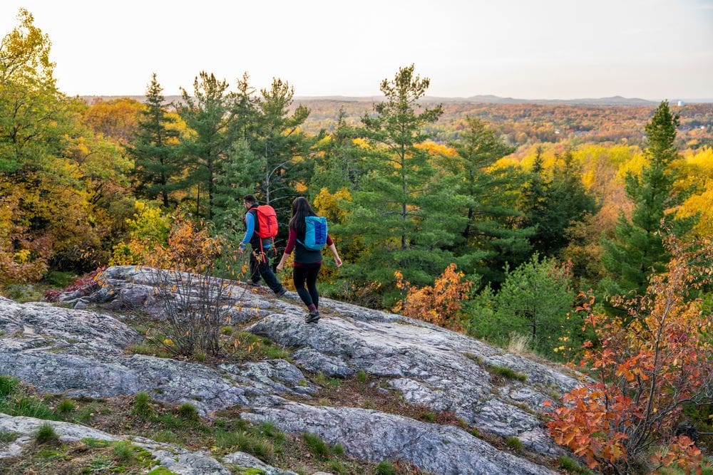 Two hikers wearing backpacks enjoy a fall hike in Marquette, Michigan, one of the best places to see fall colors in the Midwest for families.