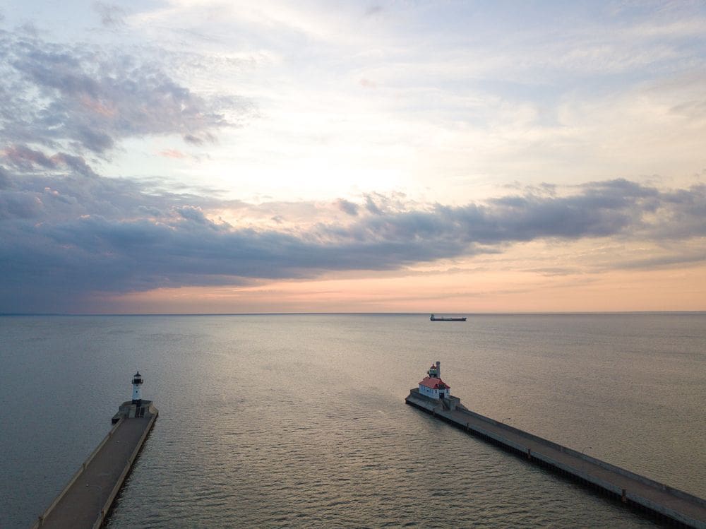 An aerial view of the Duluth port, with a lighthouse on one side and another building on the other at sunset.