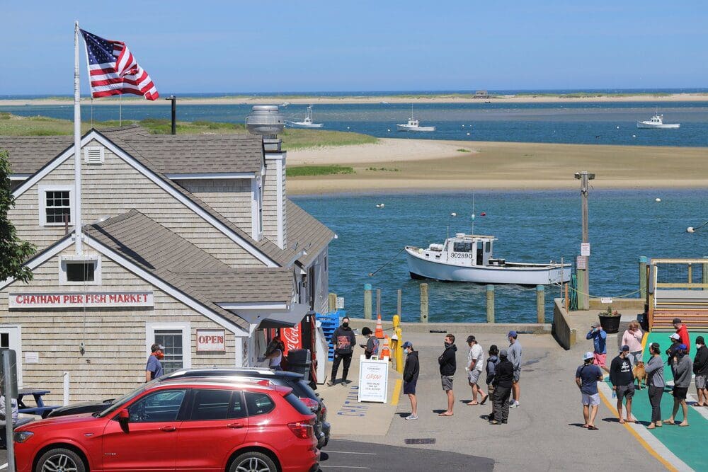 Several people mill about the Chatham Pier Fish Market on a sunny day in Cape Cod.