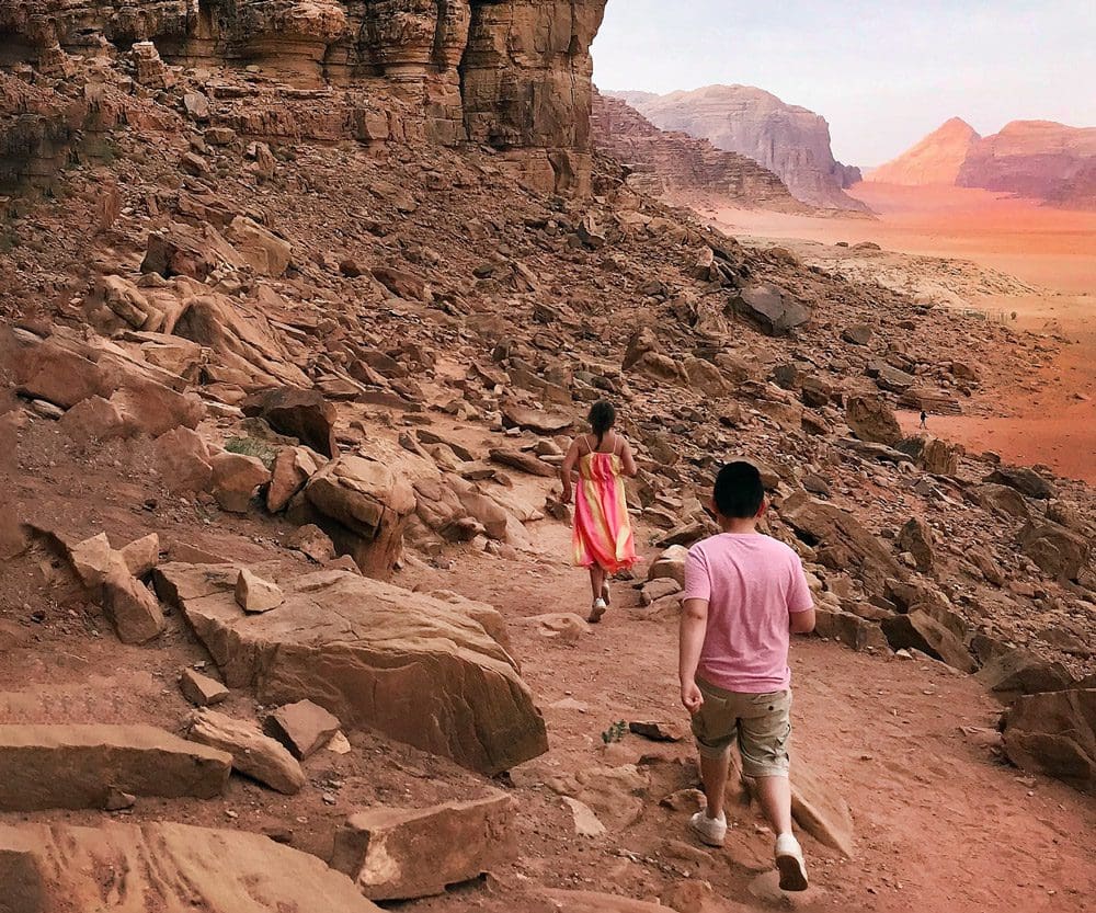 Two kids walk across a rocky terrain toward Wadi Rum.