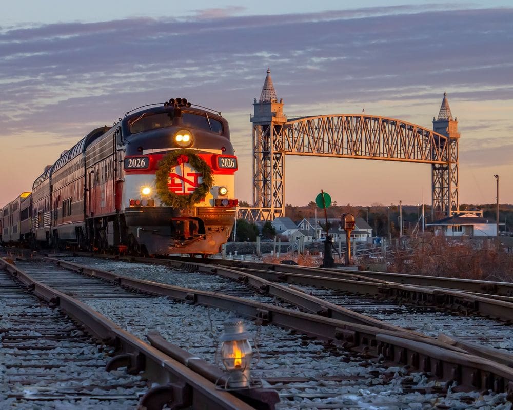 The Cape Cod Central Railroad rumbles down the tracks on a crips late autumn day, some fall foliage can be seen near the tracks.