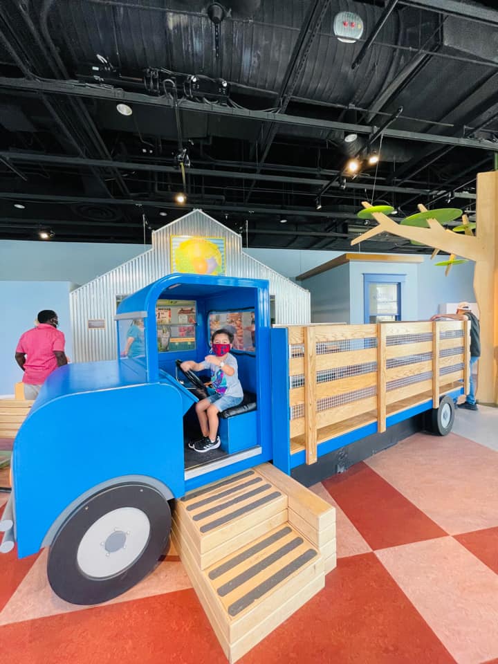 A young boy pretends to drive a farm truck at an exhibit at the Perot Museum.