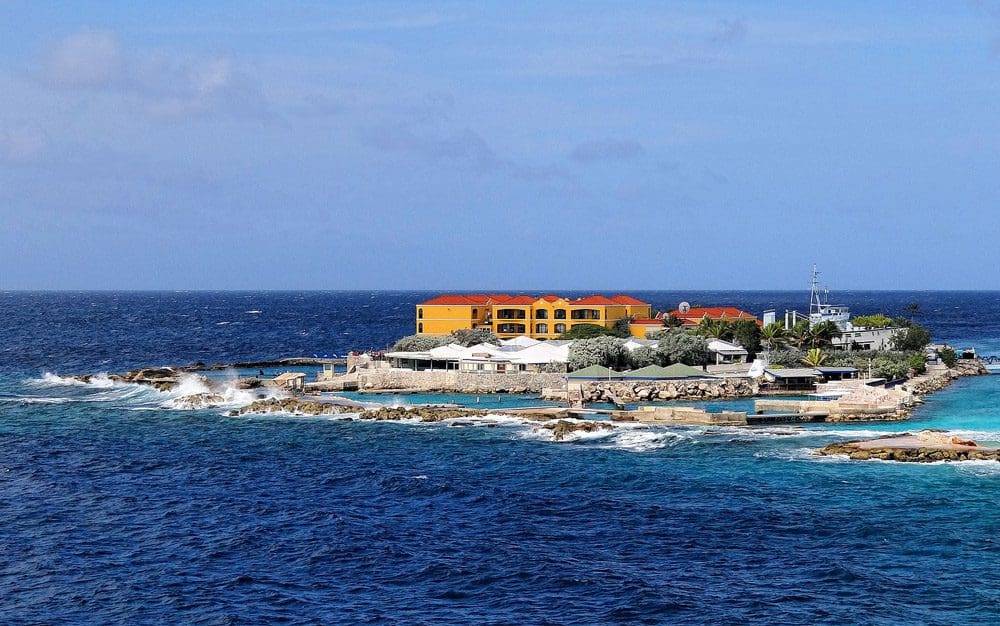 A view of the Curacao Sea Aquarium across the water, featuring a colorful building and blue sky.