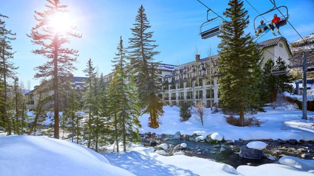 Two people ride on a chairlift over Grand Hyatt Vail on a winter day.