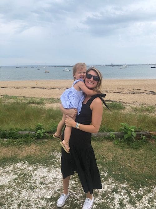 A mother holds her smiling toddler daughter on the shore of Provincetown.