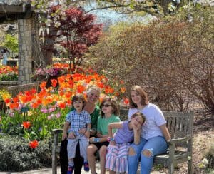 A multigenerational family poses together on a bench surrounded by beautiful flowers at the The Dallas Arboretum And Botanical Garden.
