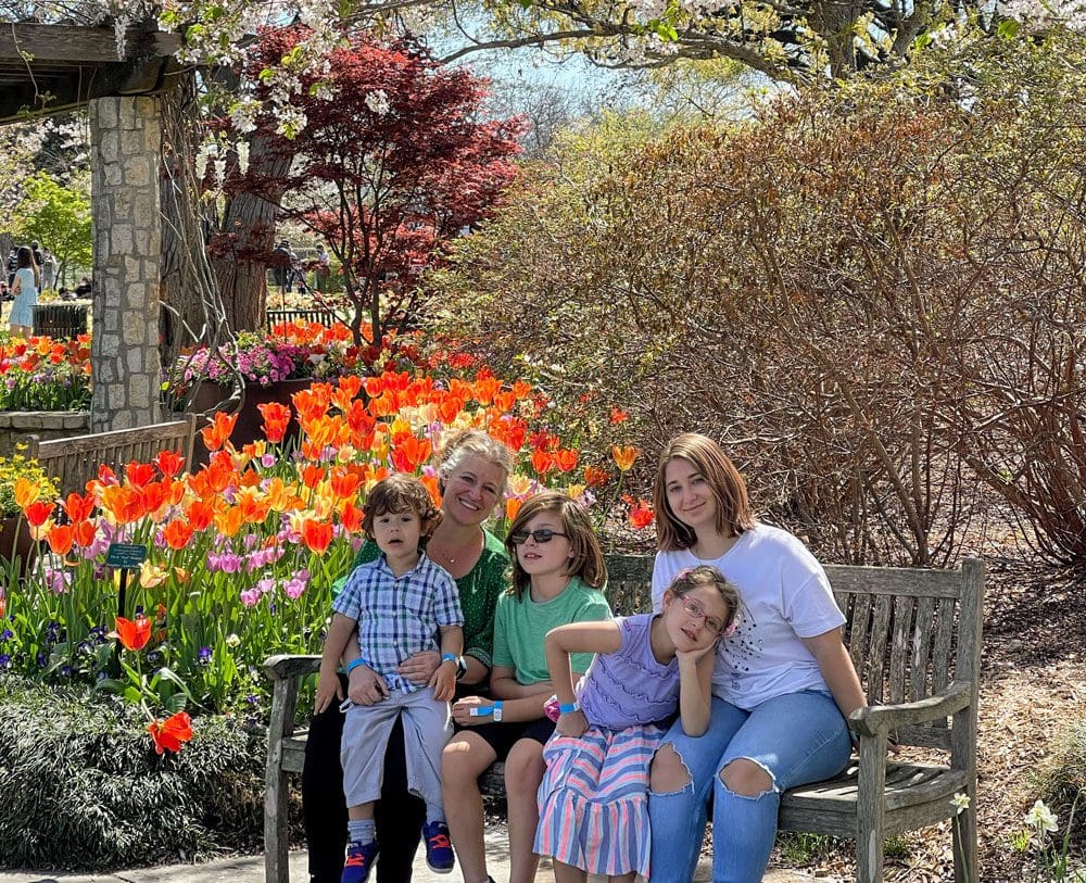 A multigenerational family poses together on a bench surrounded by beautiful flowers at the The Dallas Arboretum And Botanical Garden.