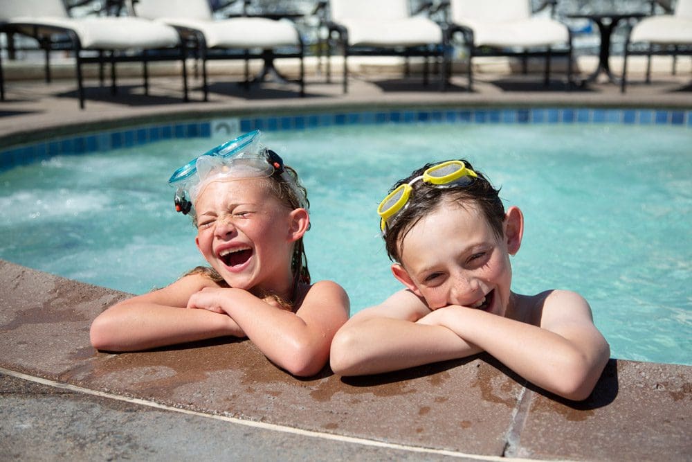 Two kids laugh while crossing their arms over the edge of the pool at Kona Kai Resort & Spa.