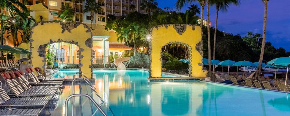 The still, turquoise pool at the Marriott’s Frenchman’s Cove at night, surrounded by colorful yellow walls.