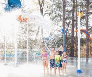 Five kids stand together laughing while enjoying a large splash pad water feature at the Odetah Camping Resort.
