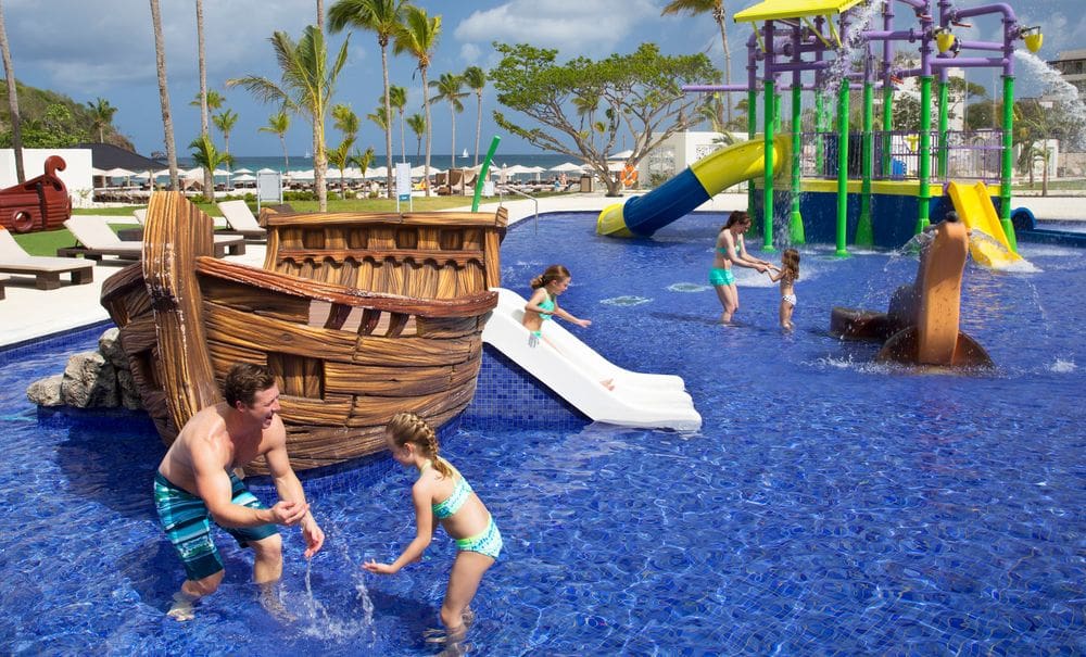 Kids playing in the splash pad at Royalton Saint Lucia Resort and Spa, featuring a pirate ship and two slides.