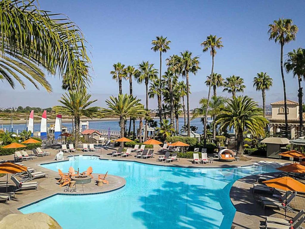 A view of the pool, surrounded by tall palm tress and orange pool loungers, at the San Diego Mission Bay Resort, one of the best San Diego beachfront hotels for families.