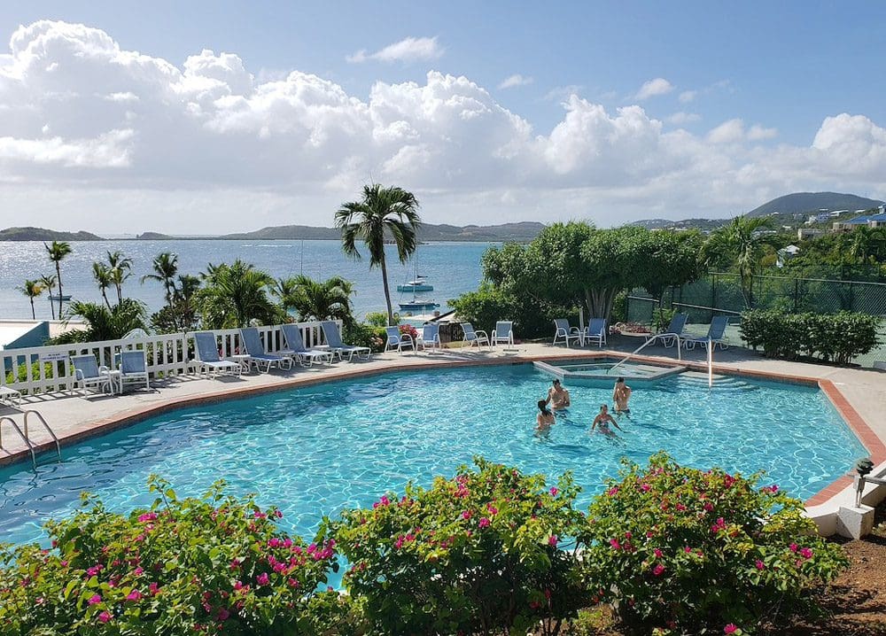 A family plays in the pool at the Secret Harbour Beach Resort, with a view of the ocean in the distance.