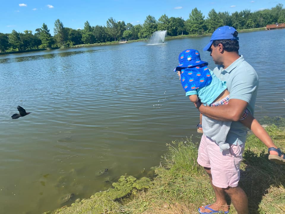 A dad holds his young son while they enjoy a beautiful day along the shore of a pond at Russel Creek Park in Dallas, Texas.