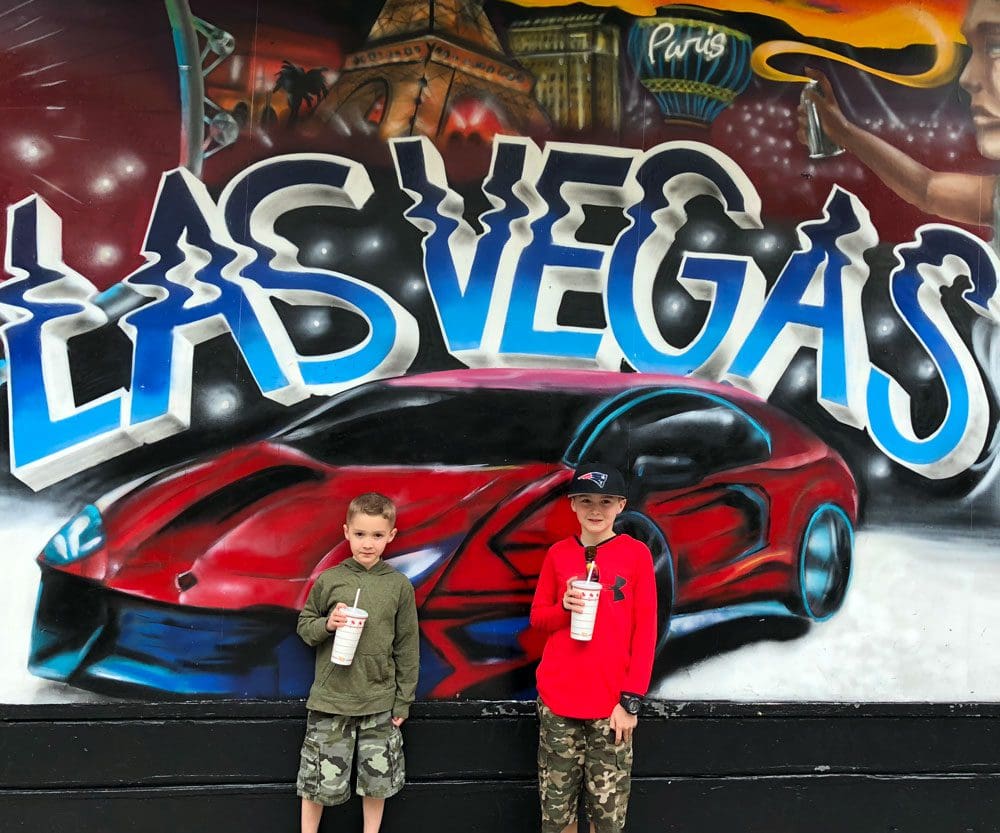 Two Kids stand in front of a graffiti design of a fast red card and the words "Las Vegas".