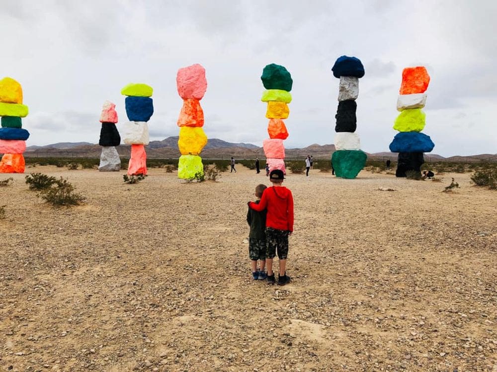 Two kids stand together looking at the Seven Magic Mountains in the desert near Las Vegas.