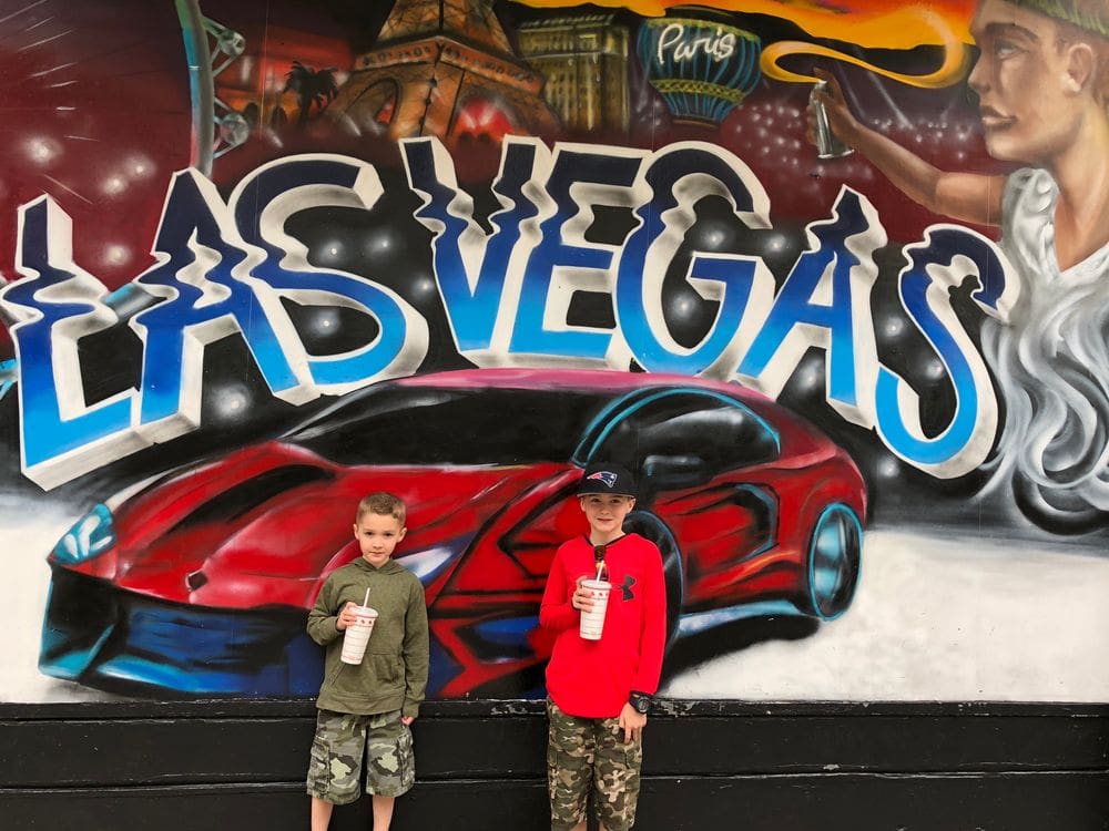Two Kids stand in front of a graffiti design of a fast red card and the words "Las Vegas".