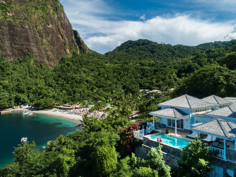 An aerial view of the beach at Sugar Beach, A Viceroy Resort, with resort buildings in the foreground, including one with a terrace pool.