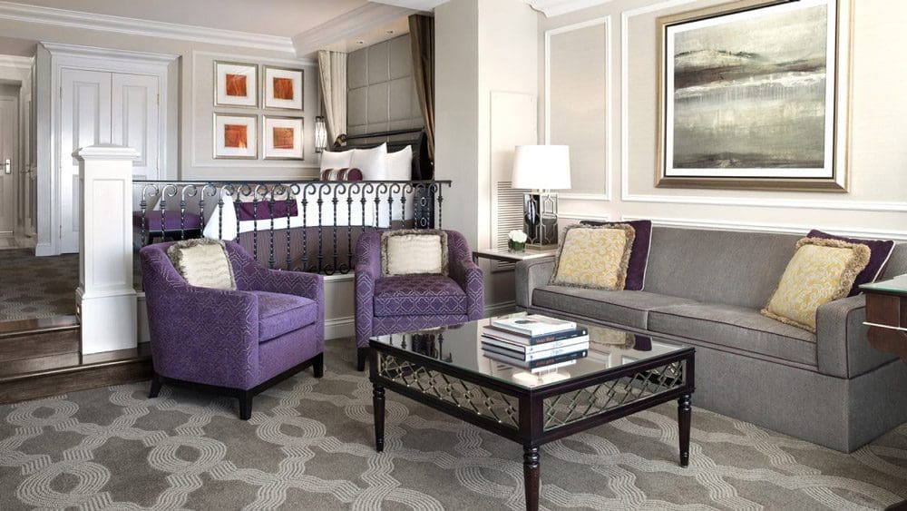 Inside one of the stylish suites at the The Venetian Resort®, featuring a purple set of chairs, grey couch, and coffee table.