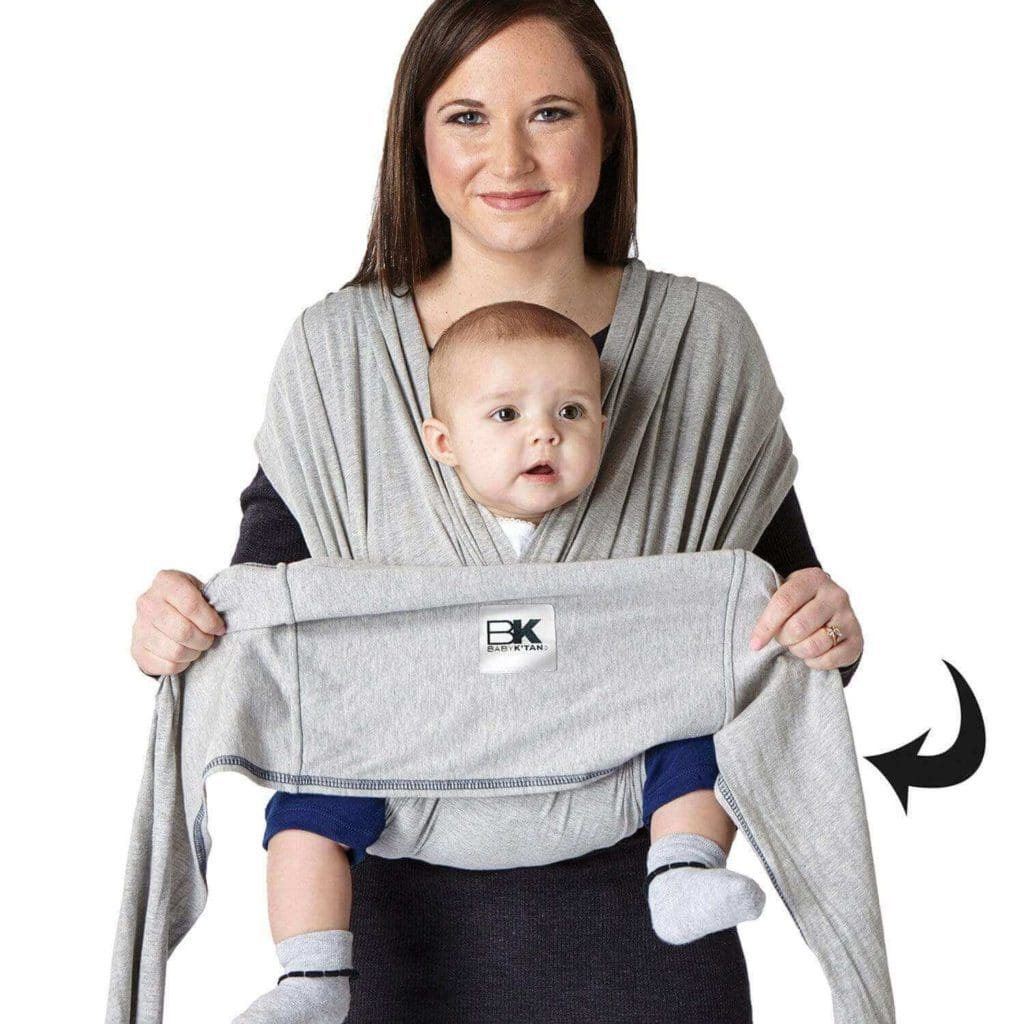 A woman demonstrates the ease of using the straps of the Baby K'tan Baby Carrier, while carrying her baby on her front, one of the best Best baby carriers for travel.