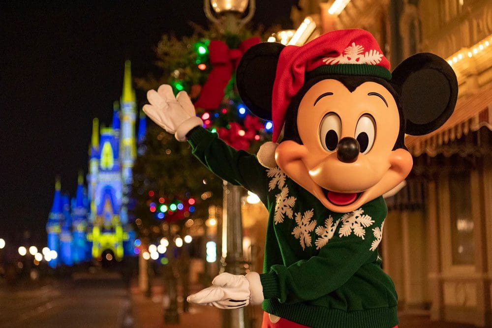 Mickey Mouse shows off Magic Kingdom's castle during the holidays, while wearing a green sweater and red Santa hat.