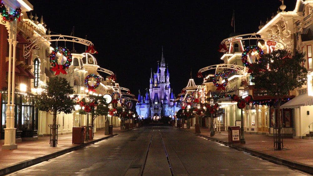 An empty Main Street leading to Cinderella's castle at Magic Kingdom, all decorated and lit up at night during the holidays.
