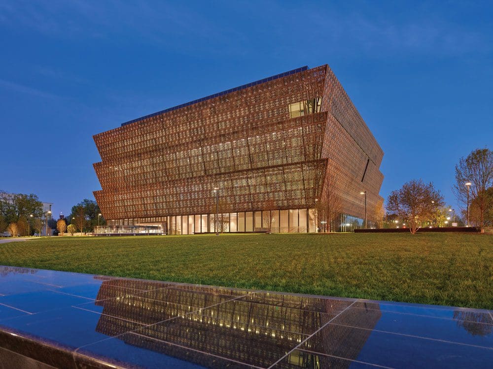 A view of National Museum of African American History and Culture, across a small fountain at night.