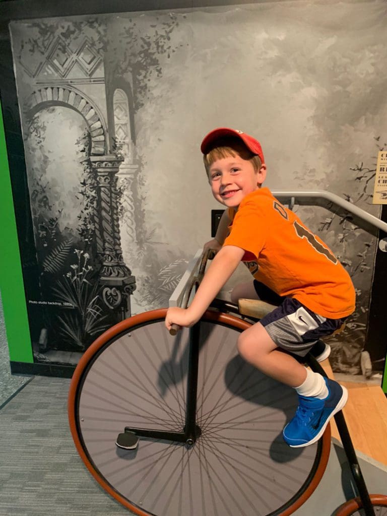 A young boy pretends to ride an old-fashion bike at an exhibit at the Smithsonian National Museum of American History.