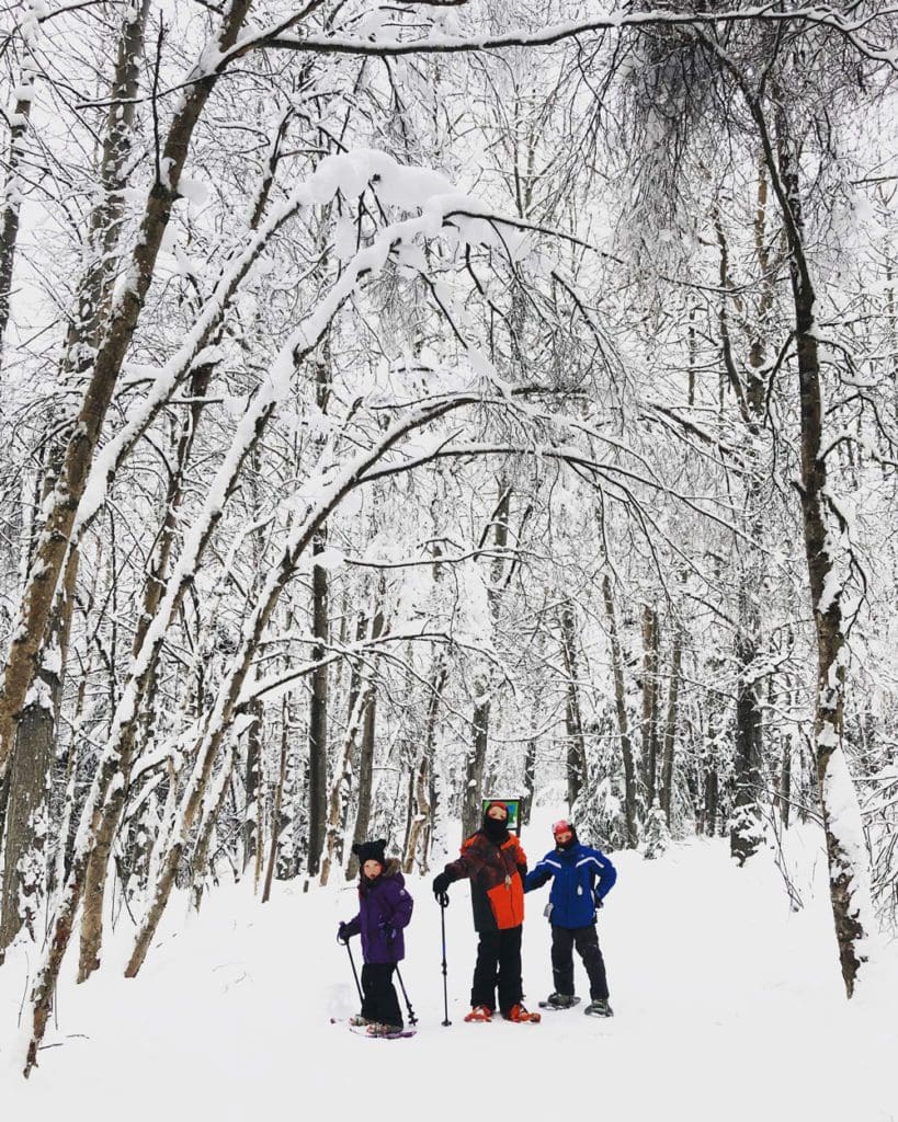 Three kids snowshoe along Eagle River Nature Center near Anchorage.