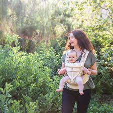 A woman holds her child in a front carrier by Ergobaby Omni 360 All-Position Baby Carrier, with lush greenery behind her.