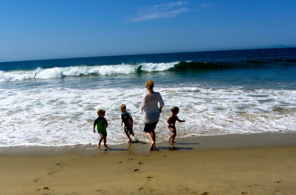 A mom and her three kids run along the beach and waves in San Diego, one of the best Thanksgiving destinations in the United States for families.
