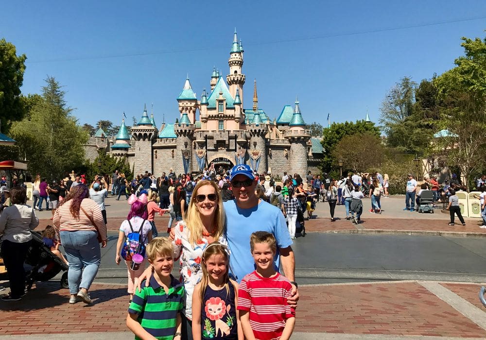 Two parents and their three kids stand together with the Disneyland castle behind them. This is surely one of the best places to visit in California with kids!