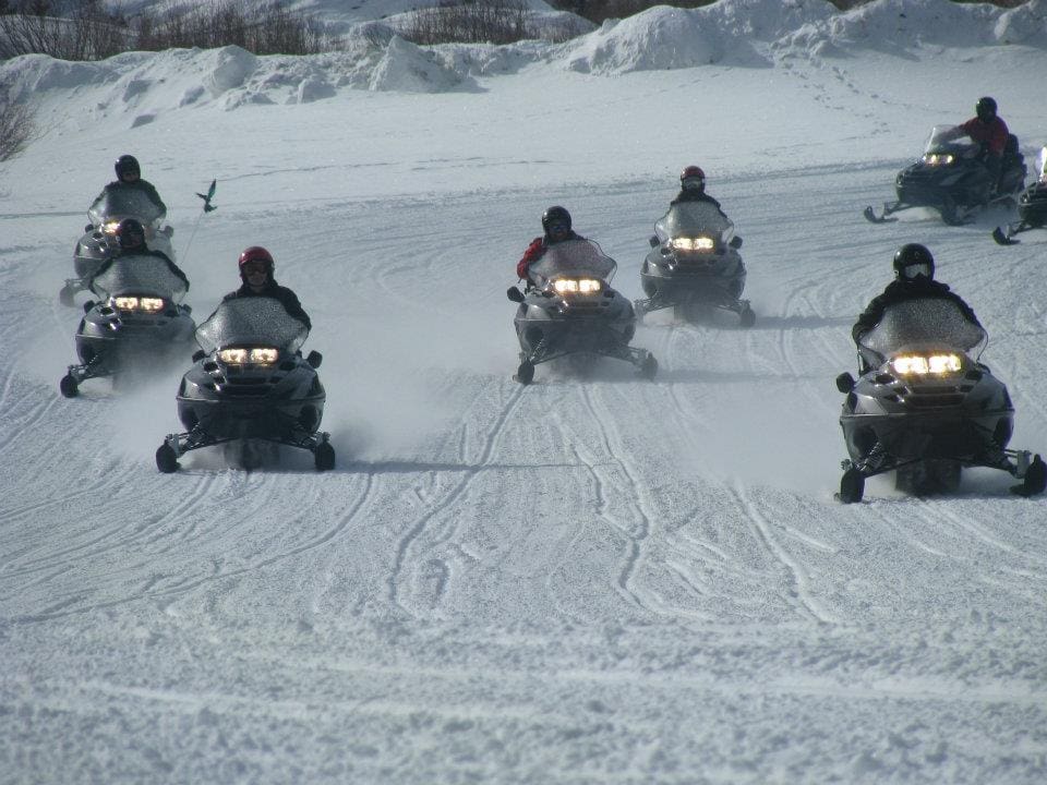 Seven snowmobilers race across a wintery open field.