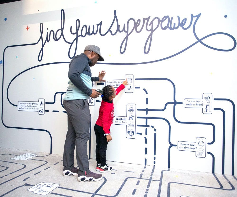 An African American man and his daughter interact with a hands-on exhibit about super powers at the National Children’s Museum.