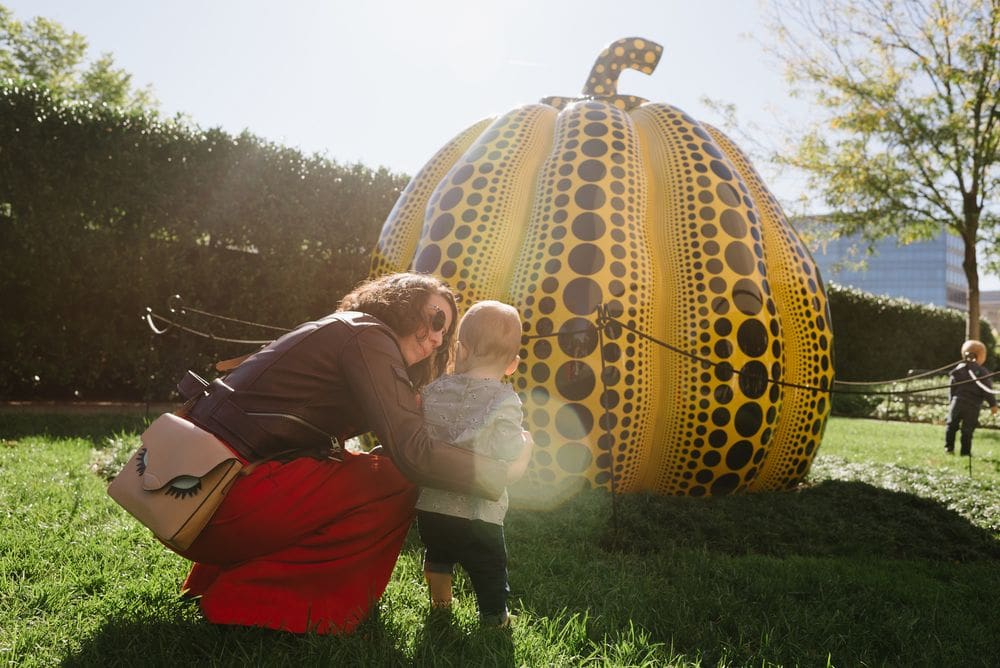 A mom and toddler look at an outdoor exhibit of a large pumpkin at the Hirshhorn Museum and Sculpture Garden.