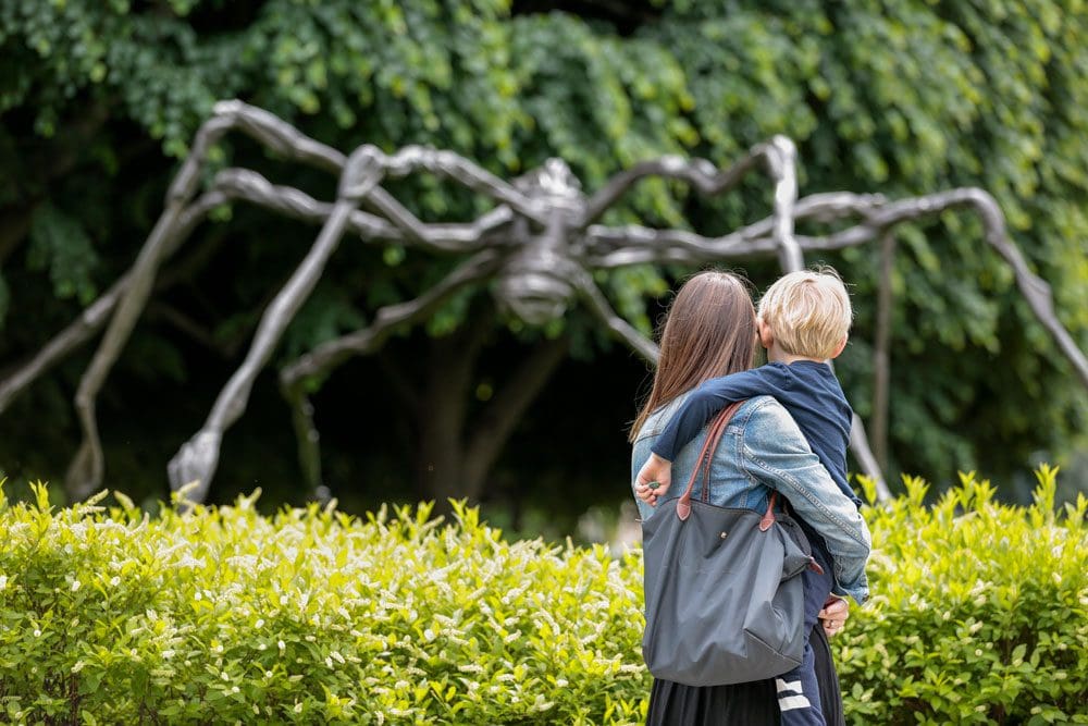 A mom holds her young son as they view an outdoor exhibit shaped like a huge spider at the National Gallery of Art and Sculpture Garden.
