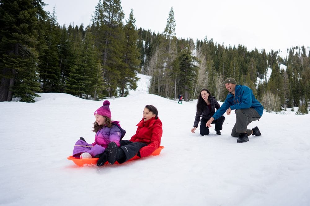 Two parents look on excitedly as two of their kids ride together on a sled down a snowy hill in North Lake Tahoe.