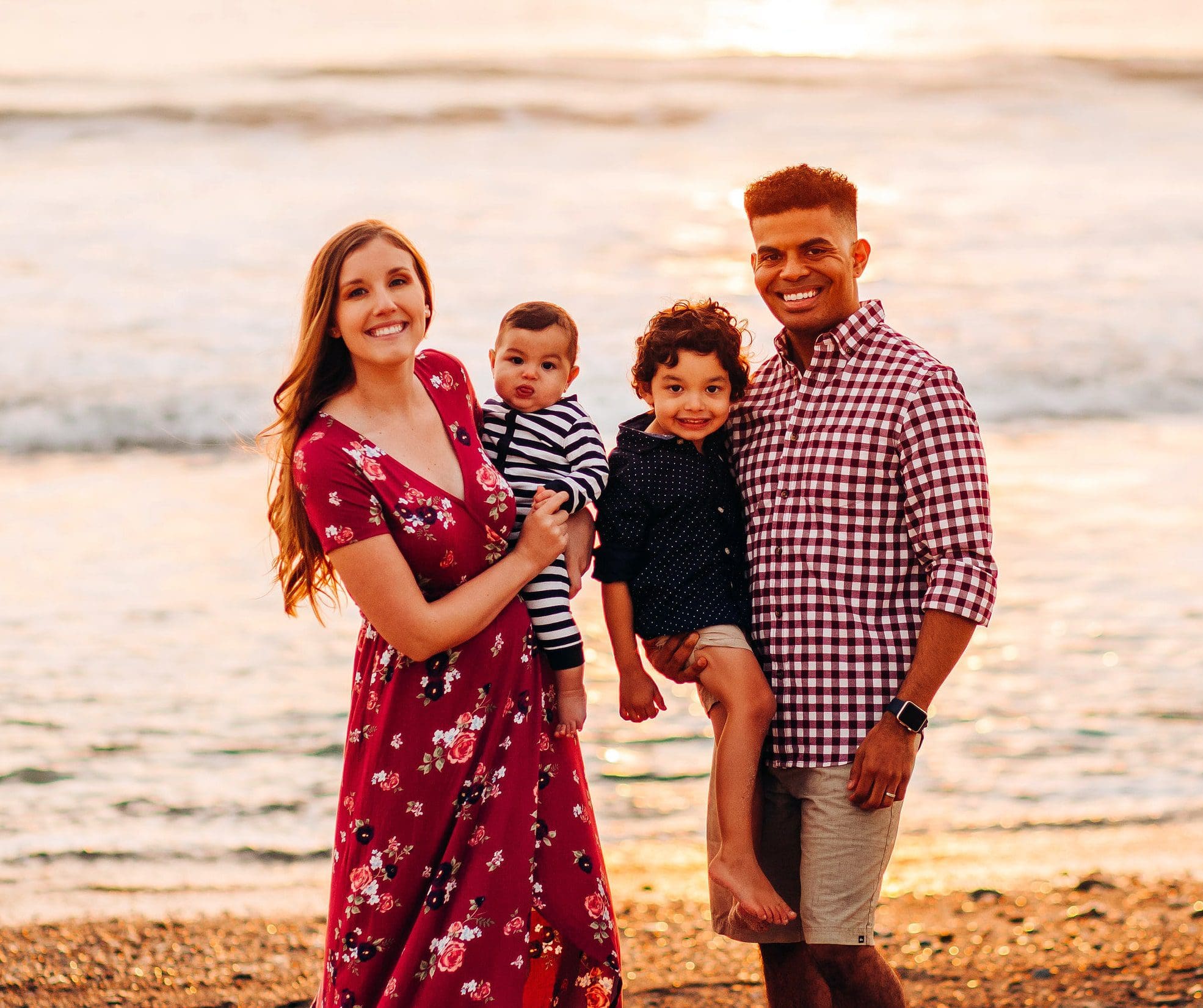 Beautiful family posing for photo in front of the ocean and sunset.