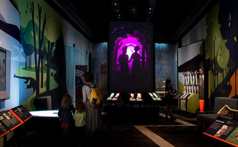 A mom and her two young children look at an exhibit in a darkened room at the Smithsonian National Museum of the American Indian.