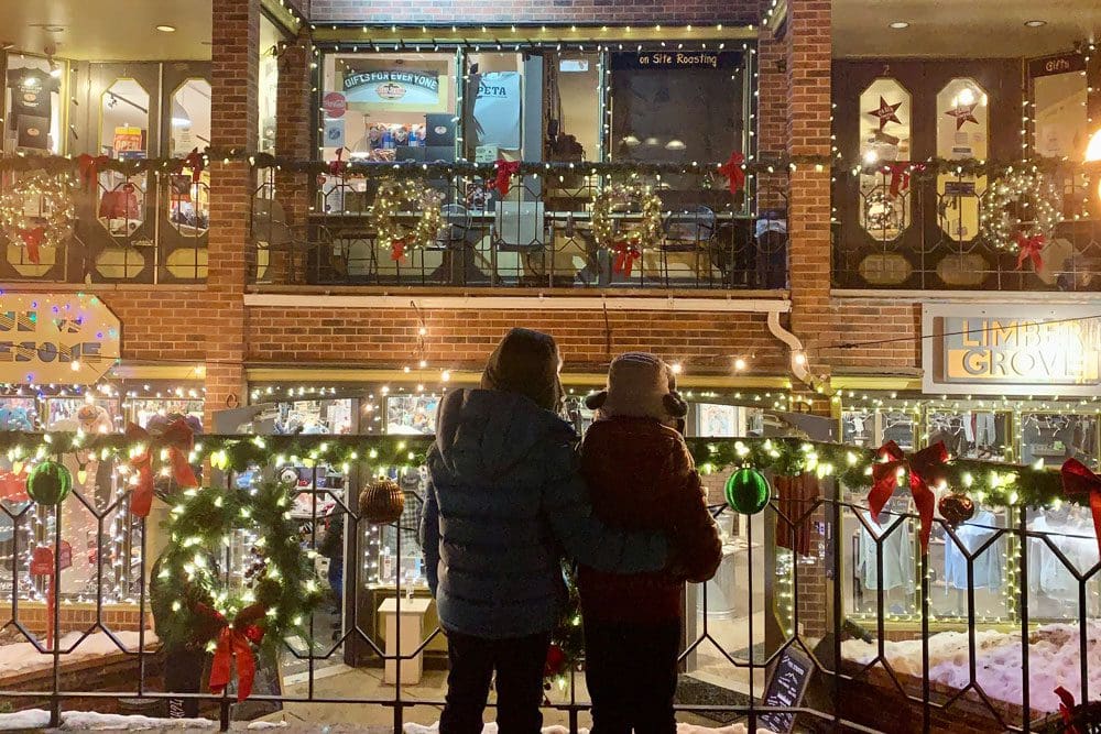 Two kids in winter gear stand together looking out onto the holiday decorations in Breckenridge, one of the best places for a White Christmas in the United States for families.