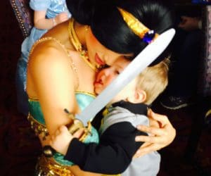 Princess Jasmine hugs a young boy dressed as a prince holding a sword at Disney World.