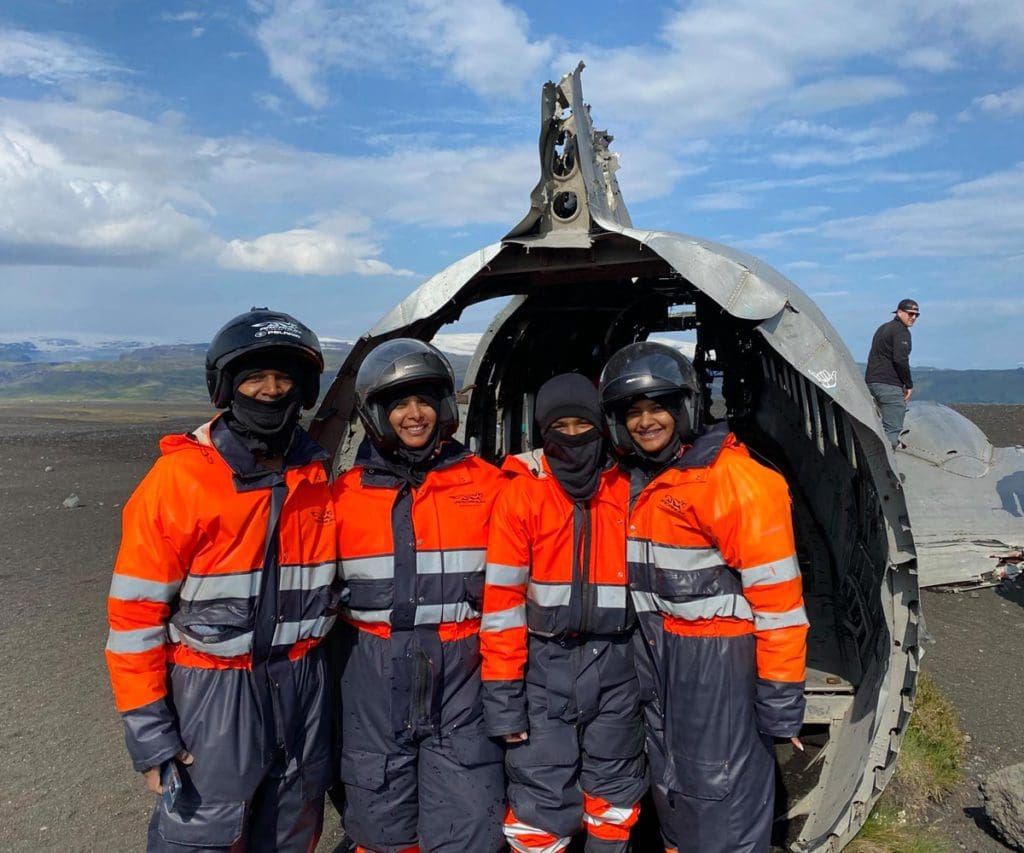 Four people in warm gear stand in front of the Sólheimasandur Plane Wreck.