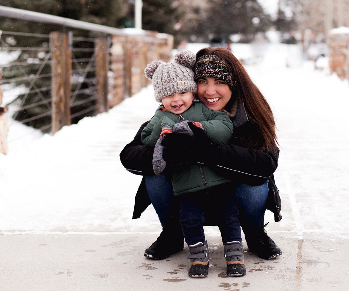 A mom hugs her toddler while taking a walk along a snowy pedestrian bridge in Breckenridge.