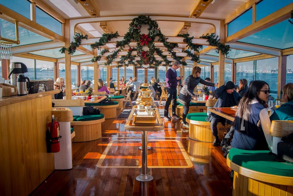 Inside the Skyline Holiday Cocoa Cruise, featuring several people seated and enjoying the views surrounded by Christmas decor, one of the best New York City Christmas activities with kids.