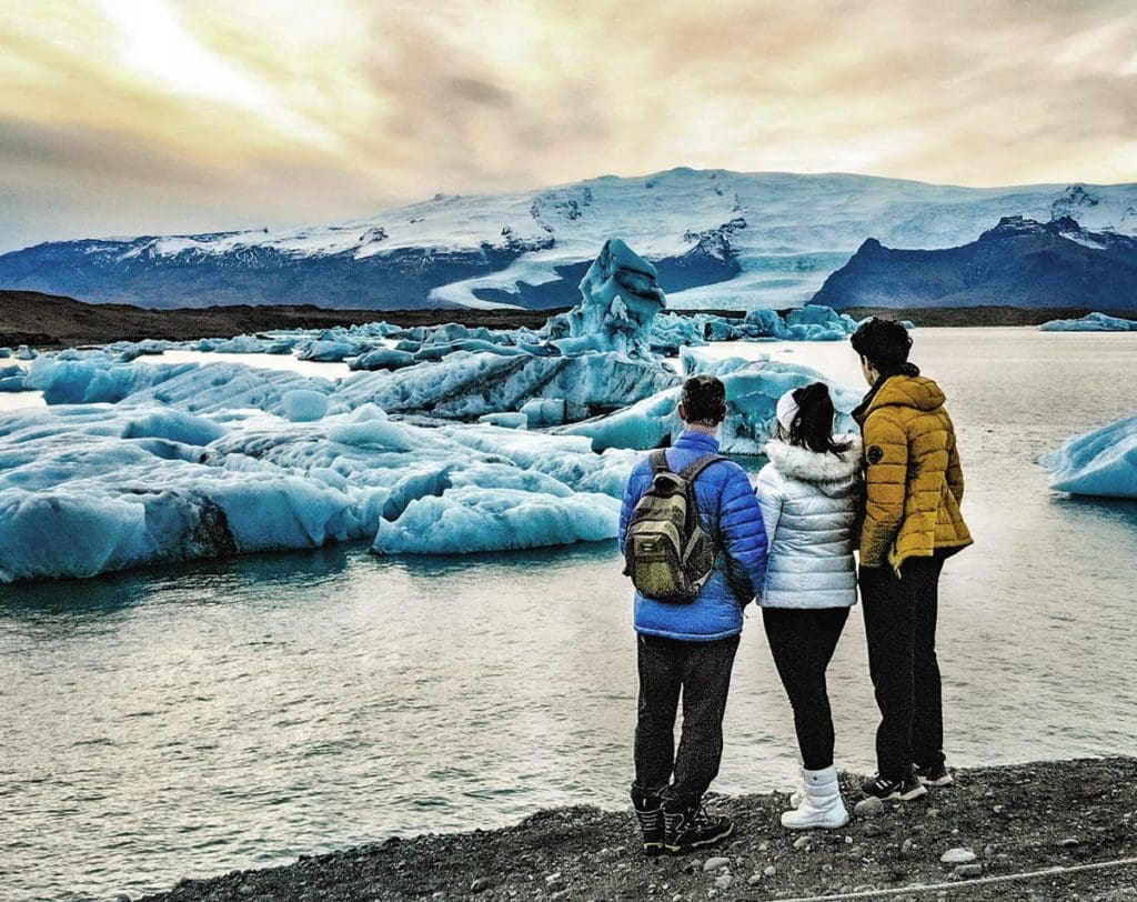 Three teens stand together looking at the Jökulsárlón Glacier Lagoon.
