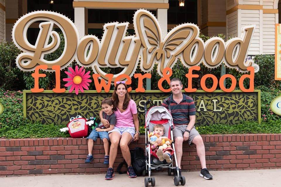 A family of four sits outside, in front of the sign for Dollywood Flower & Food in Tennessee, one of the top places in travel in 2023 with kids.