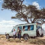 Parents stand near a safari jeep, while their kids sit inside, during a safari in Tanzania.