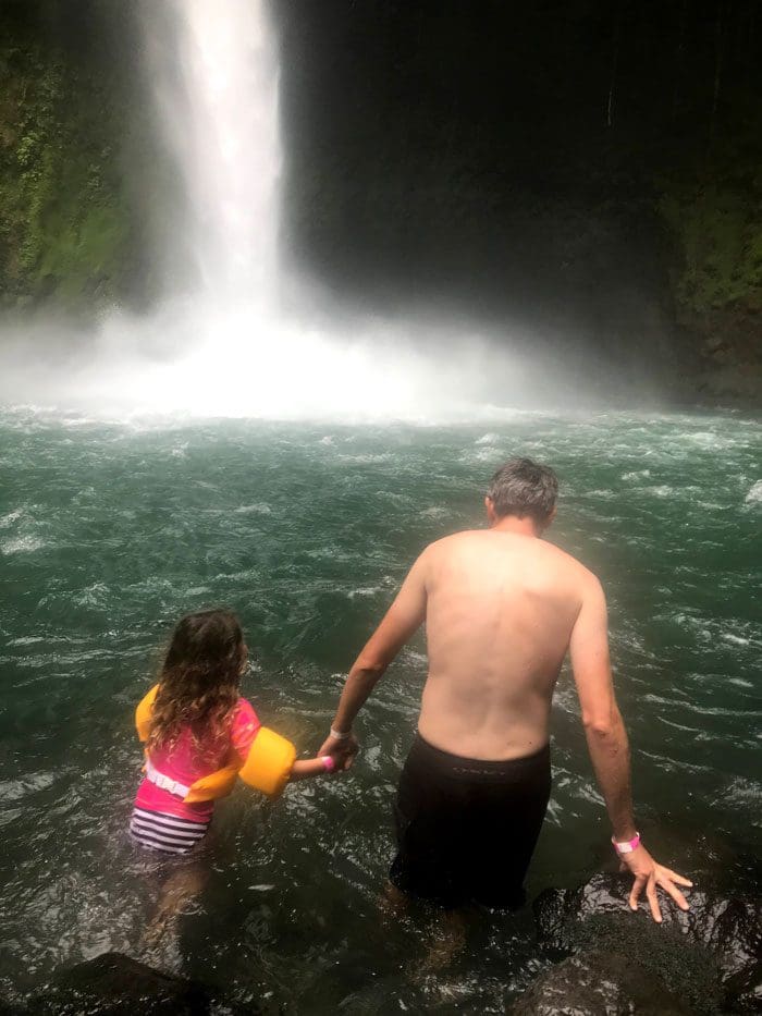 Dad and daughter wade into the water below the La Fortuna Watefall.