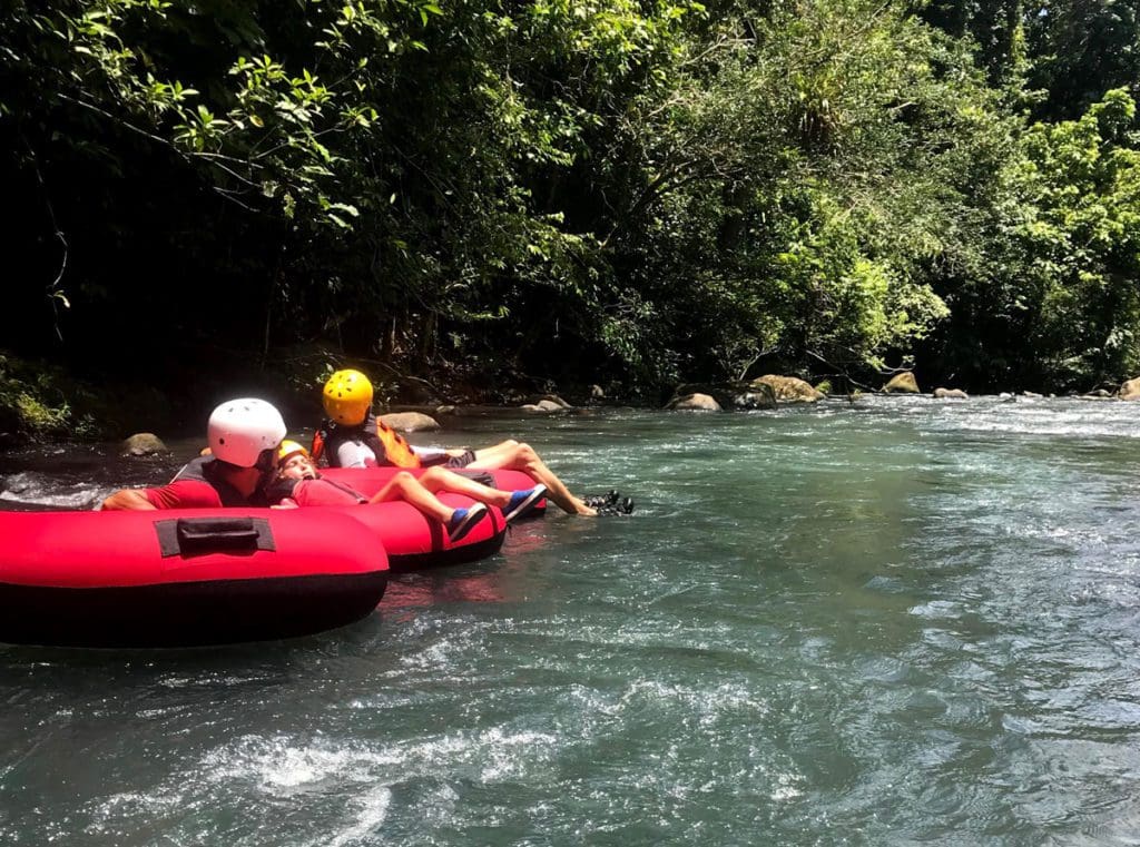 A family floats down Rio Celeste on large red tubs in Costa Rica.