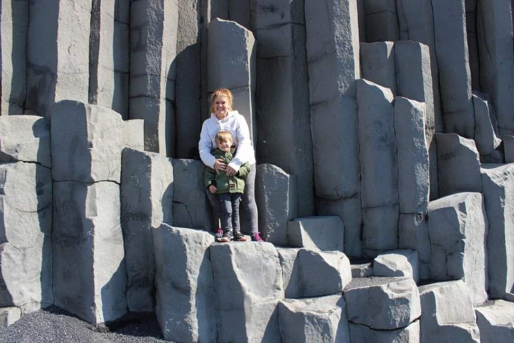 A mom and her young son stand together amongst the iconic rock formations at the Black Beach in Iceland.